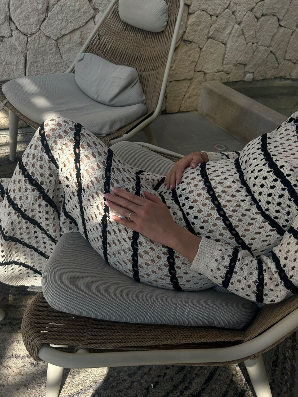 Nahaufnahme eines gestreiften Strickkleids über dem Babybauch, Hand auf dem Bauch